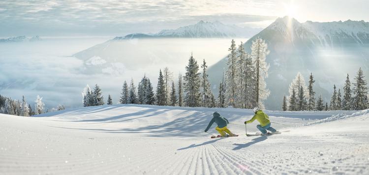 two skiiers skiiing down mountain ski slope with clouds in background