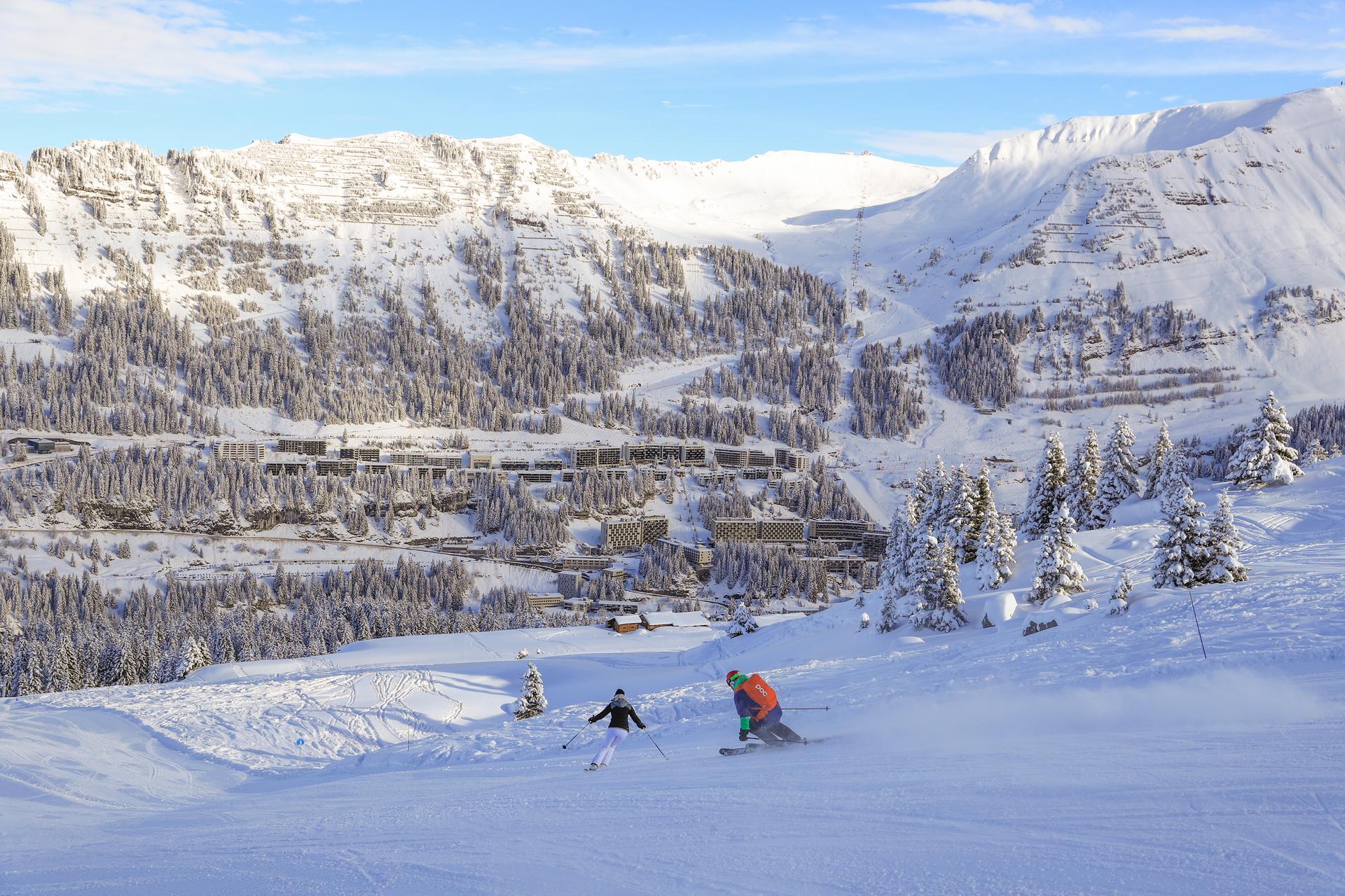 Skiiers skiing down slope into Flaine ski resort on bluebird day